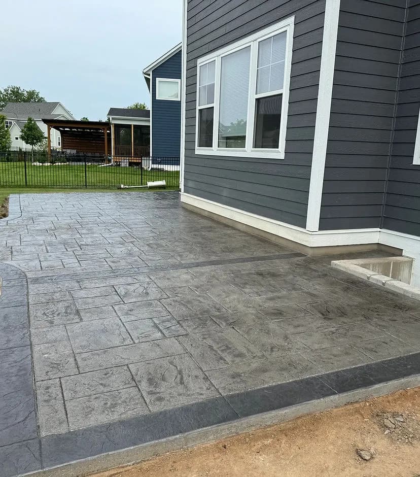 Stylish stamped concrete patio beside a modern gray house with a landscaped yard.