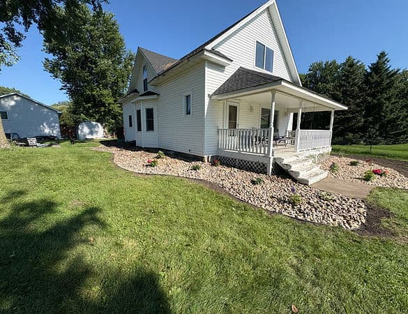 Charming white house with porch, landscaped yard, and gravel pathway on a sunny day.