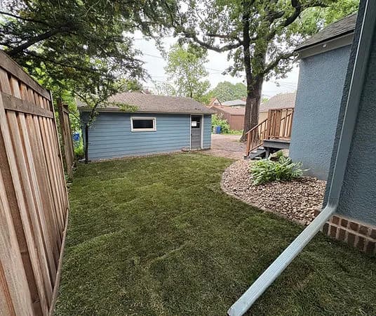 Lush green backyard with newly laid sod, wooden fence, and blue garage in suburban setting.