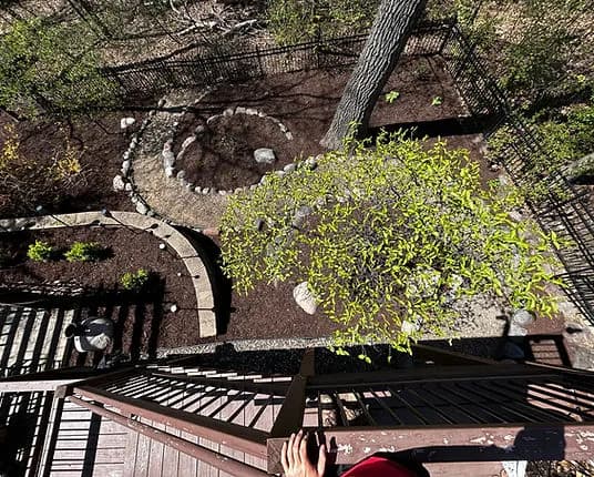 Aerial view of a landscaped garden with a spiral path, stones, and a tree, from a balcony.