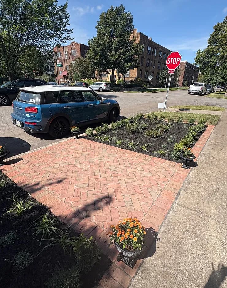 Blue Mini Cooper parked beside a landscaped garden and a stop sign in an urban setting.