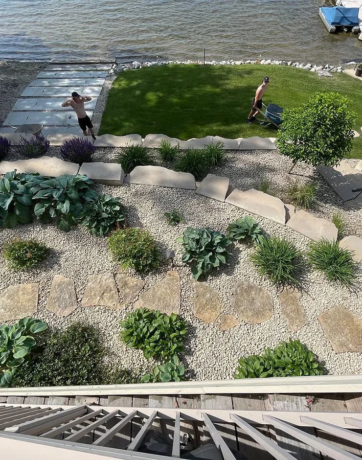 Aerial view of a landscaped backyard by the water with two people gardening.