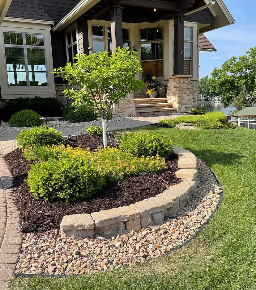 Beautifully landscaped garden with shrubs, stones, and a tree leading to a lakefront home.